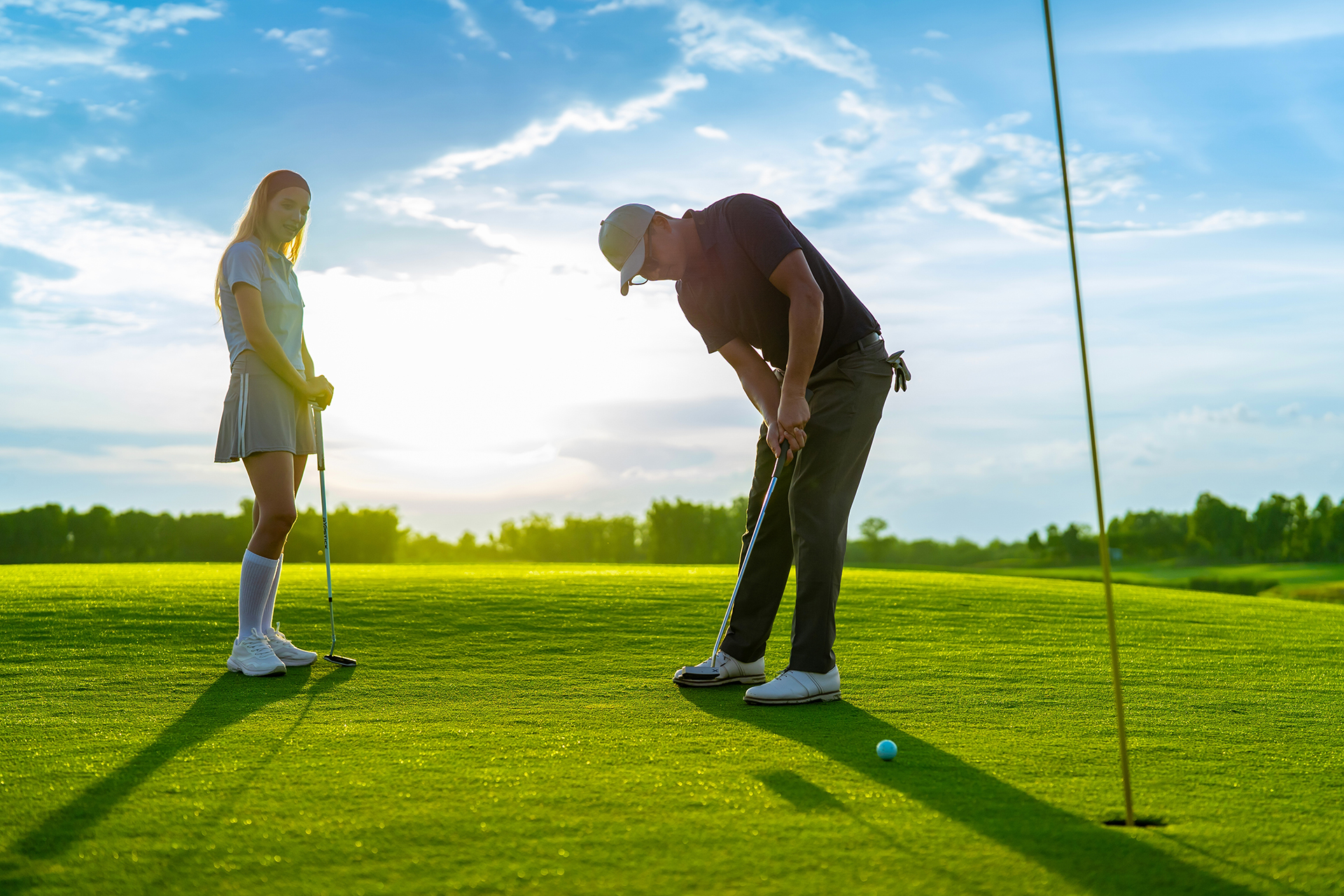 Asian,man,and,woman,golfers,swing,clubs,together,on,scenic