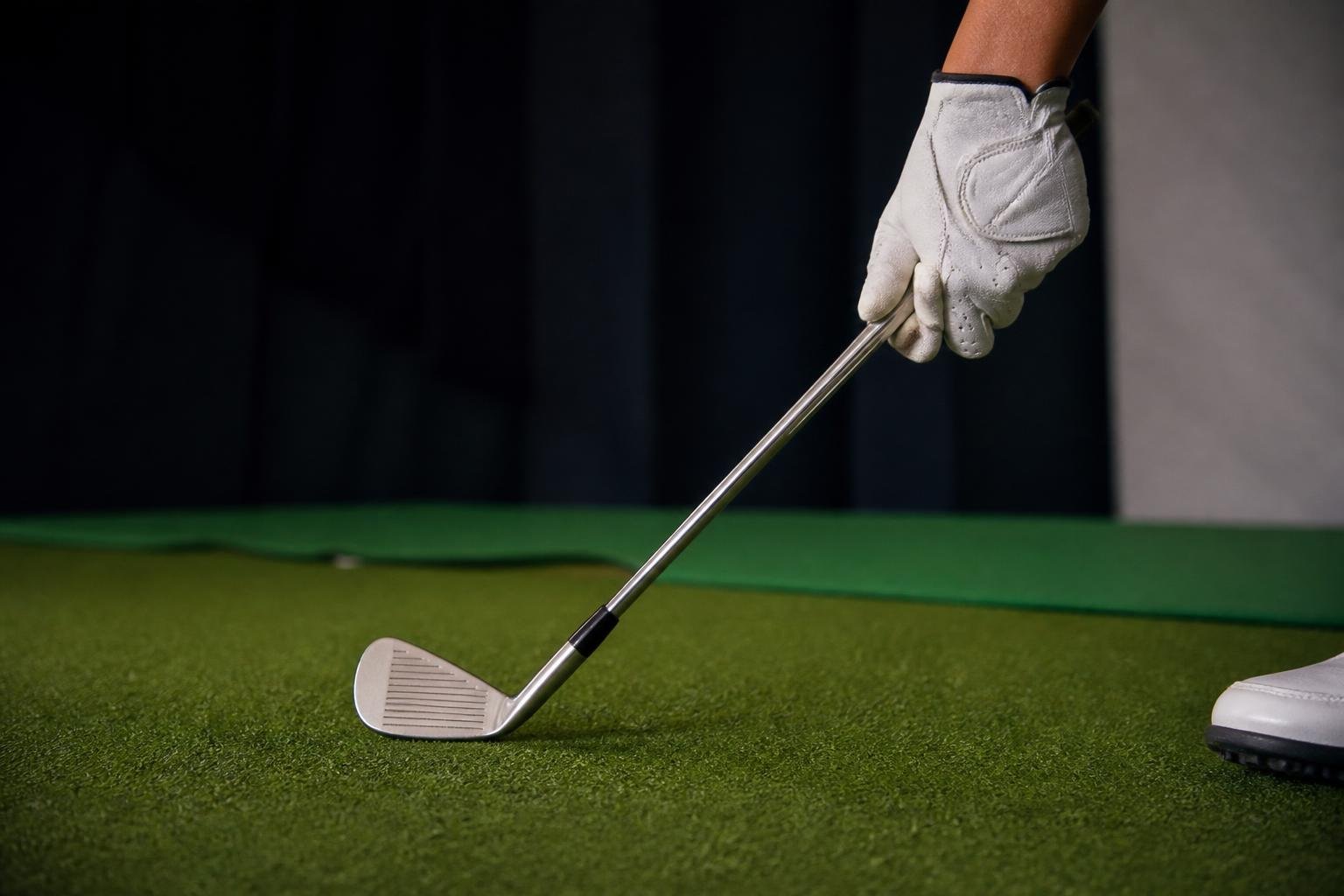 Ultra-realistic photograph of a golfer's gloved hand gripping an iron at address on an indoor hitting mat, soft studio lighting