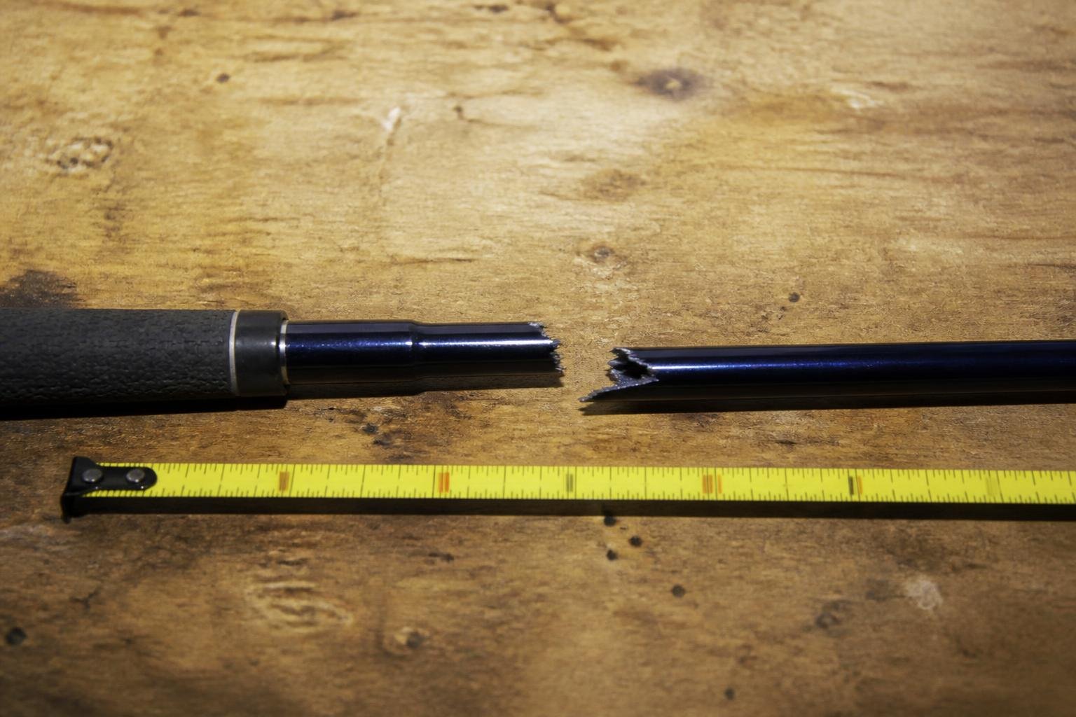 Ultra-realistic photograph of a snapped golf shaft laid on a workbench next to a measuring tape, documentary style, natural light