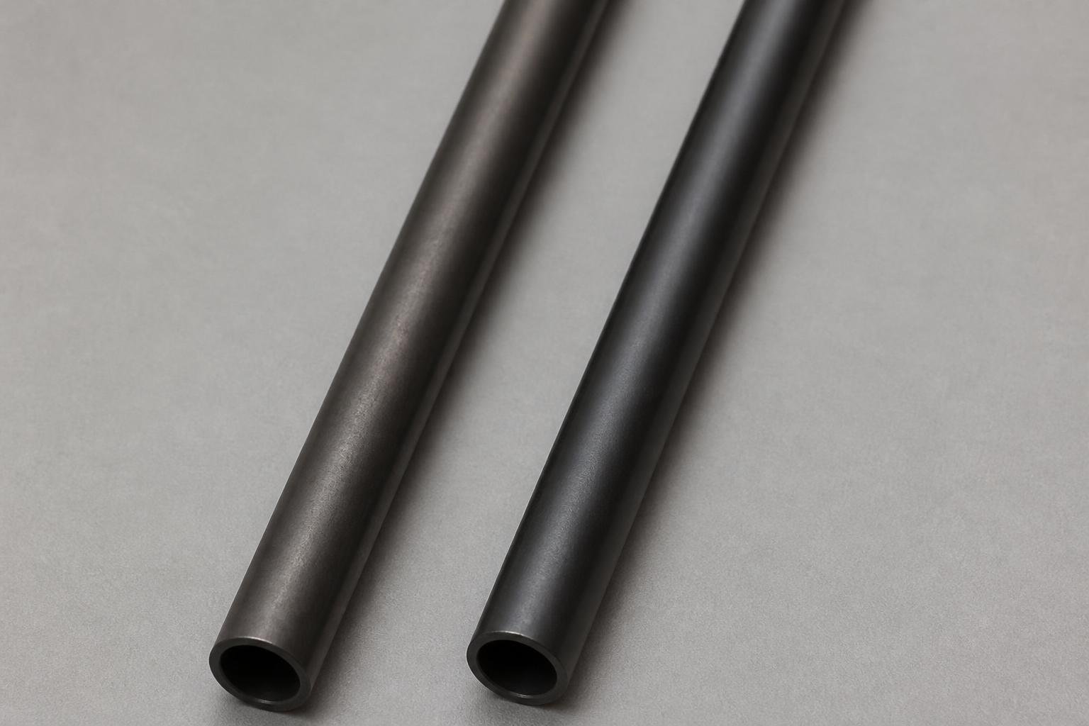 bright even studio lighting. Two iron shafts with slightly different dark finishes laid side by side on a clean gray backdrop
