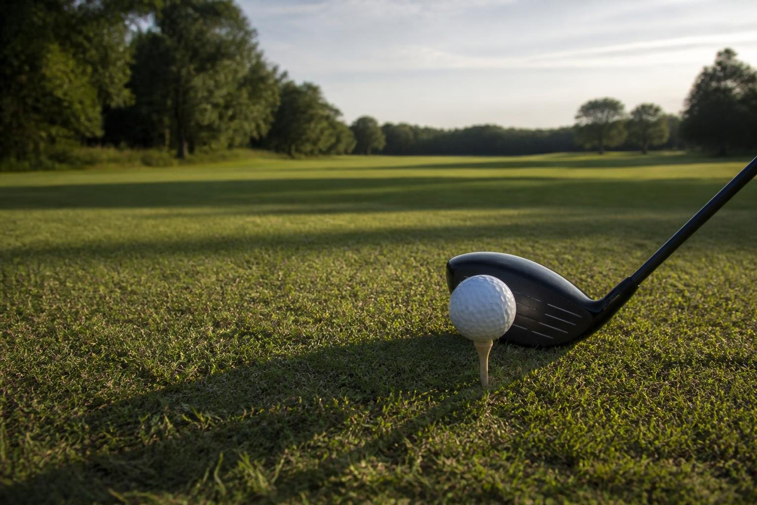 Driver head behind a ball on a tee at the edge of a fairway